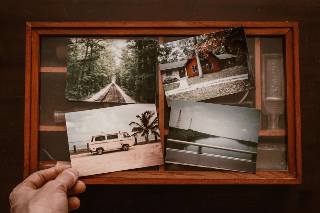En hand håller ett vintagefotografi av en folkabuss över en trälåda fylld med andra gamla bilder. En illustration av att samla minnen för att börja skriva en självbiografi.
