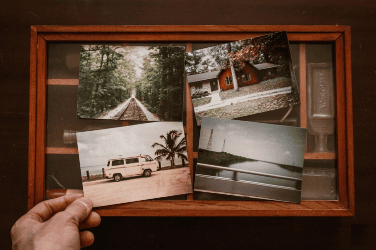 En hand håller ett vintagefotografi av en folkabuss över en trälåda fylld med andra gamla bilder. En illustration av att samla minnen för att börja skriva en självbiografi.