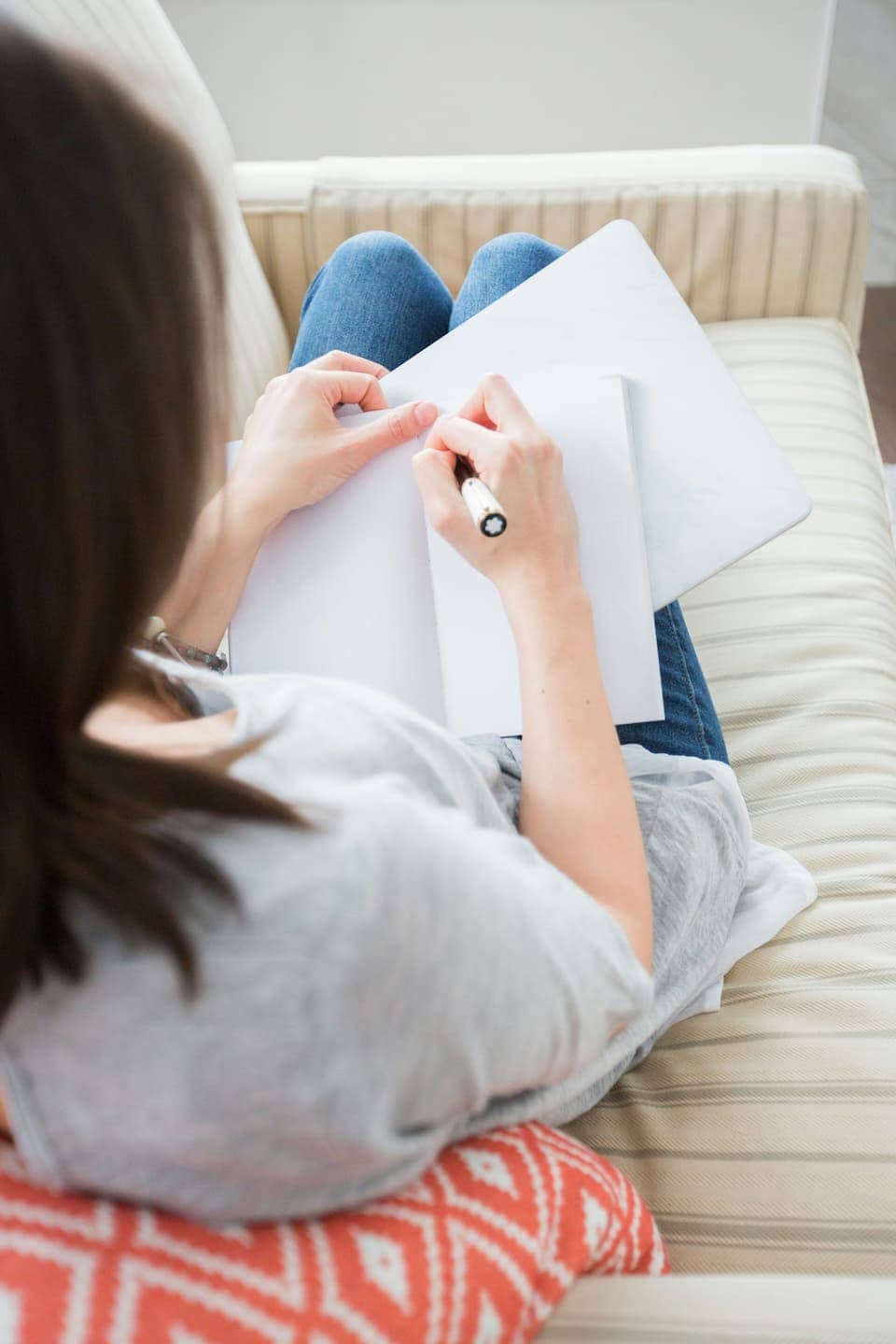 En person sedd ovanifrån som sitter i en soffa med en penna och skriver ner sina tankar och reflektioner i en anteckningsbok.